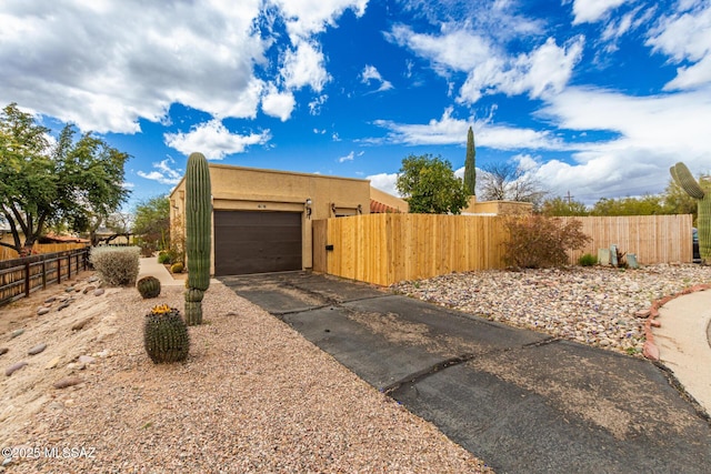 view of side of home with a fenced front yard, stucco siding, a gate, a garage, and driveway