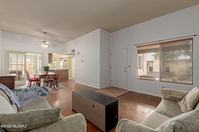 living room with ceiling fan, baseboards, and a textured ceiling