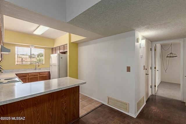 kitchen with a textured ceiling, a sink, visible vents, light countertops, and freestanding refrigerator