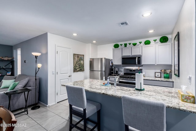 kitchen featuring a breakfast bar, a sink, stainless steel appliances, light tile patterned floors, and light stone countertops