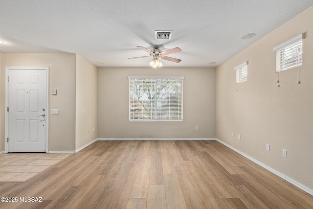 empty room featuring ceiling fan, a textured ceiling, visible vents, baseboards, and light wood-style floors