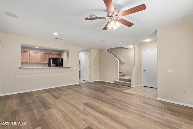 unfurnished living room featuring light wood finished floors, baseboards, visible vents, a ceiling fan, and stairs