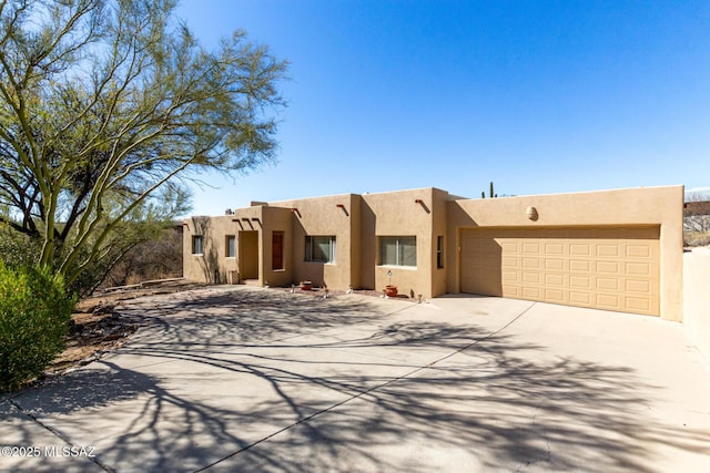 pueblo-style house with driveway, an attached garage, and stucco siding