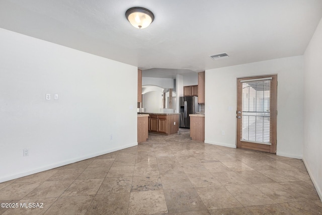 unfurnished living room with arched walkways, visible vents, and baseboards