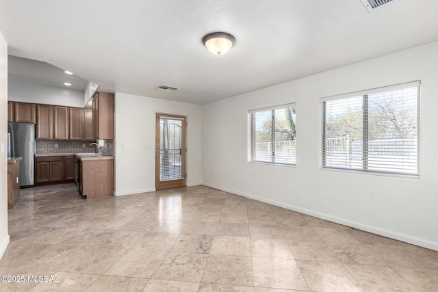 kitchen featuring tasteful backsplash, visible vents, freestanding refrigerator, open floor plan, and a sink