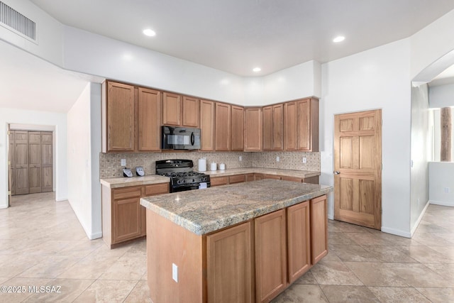 kitchen with visible vents, brown cabinets, a center island, black appliances, and backsplash