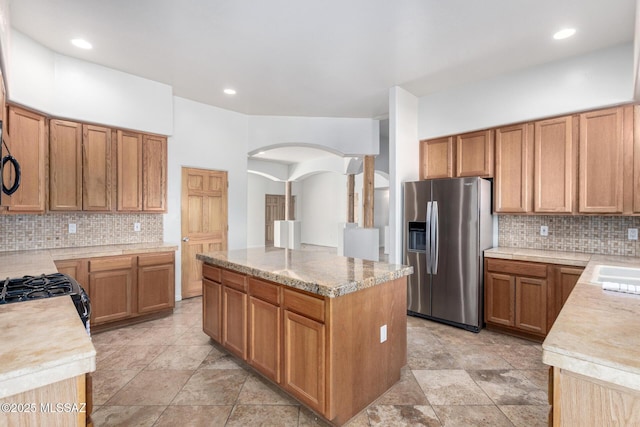 kitchen featuring tasteful backsplash, arched walkways, a center island, black appliances, and a sink