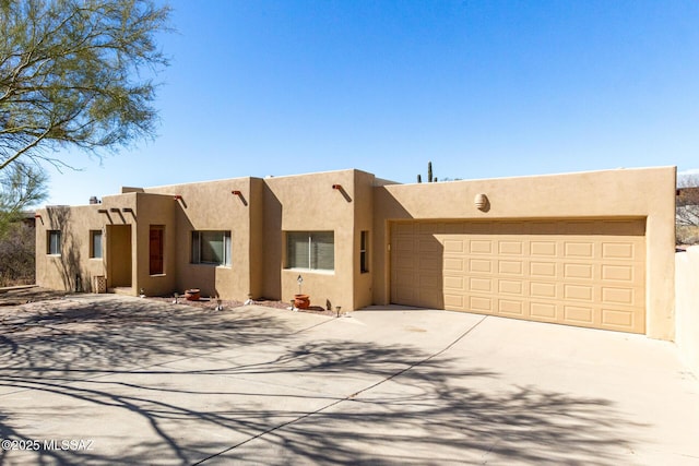 adobe home featuring a garage, driveway, and stucco siding