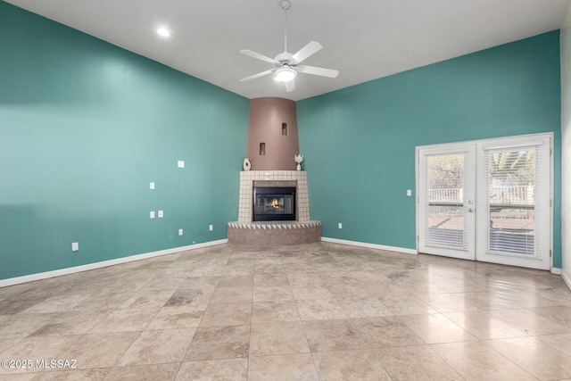 unfurnished living room featuring ceiling fan, baseboards, a tiled fireplace, and french doors