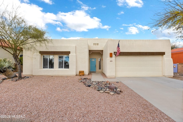 pueblo revival-style home featuring a garage, concrete driveway, and stucco siding