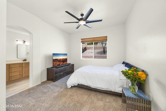 bedroom featuring ensuite bathroom, a sink, arched walkways, baseboards, and light colored carpet