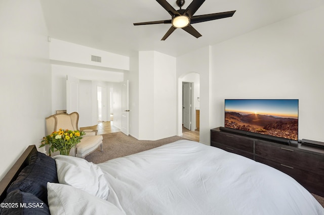 bedroom with ceiling fan, arched walkways, visible vents, and light carpet