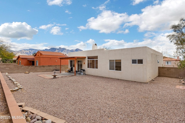 rear view of house with a fenced backyard, a chimney, stucco siding, a patio area, and a mountain view