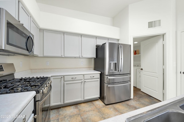 kitchen with visible vents, stainless steel appliances, light countertops, a towering ceiling, and washer and clothes dryer