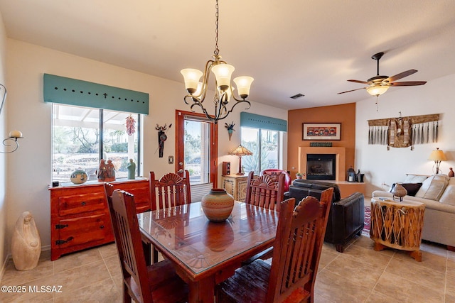 dining room featuring light tile patterned flooring, a fireplace, visible vents, and ceiling fan with notable chandelier