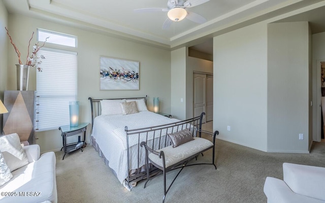 bedroom featuring a tray ceiling, a closet, light colored carpet, ceiling fan, and baseboards