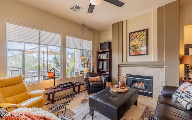 living room with a tiled fireplace, visible vents, and a ceiling fan