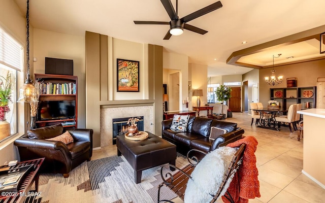 tiled living area with a tray ceiling, a fireplace, baseboards, and ceiling fan with notable chandelier