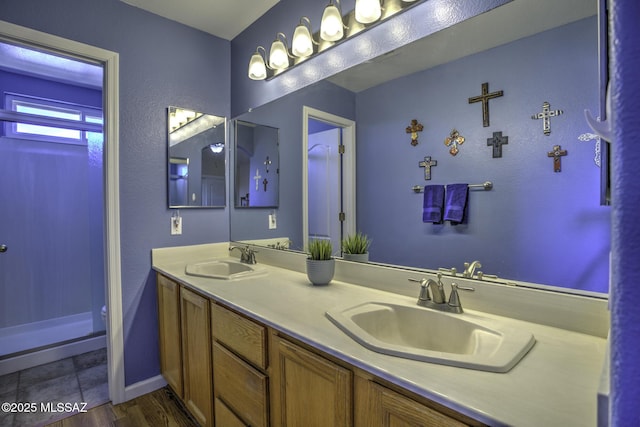 full bath featuring baseboards, a sink, a shower, and double vanity
