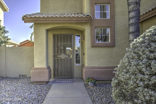 doorway to property with stucco siding, a tile roof, and fence