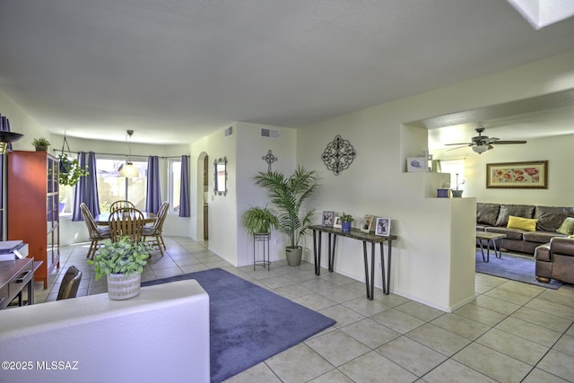 living room with a ceiling fan, visible vents, arched walkways, and light tile patterned floors
