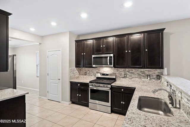 kitchen featuring a sink, light stone counters, tasteful backsplash, appliances with stainless steel finishes, and light tile patterned floors