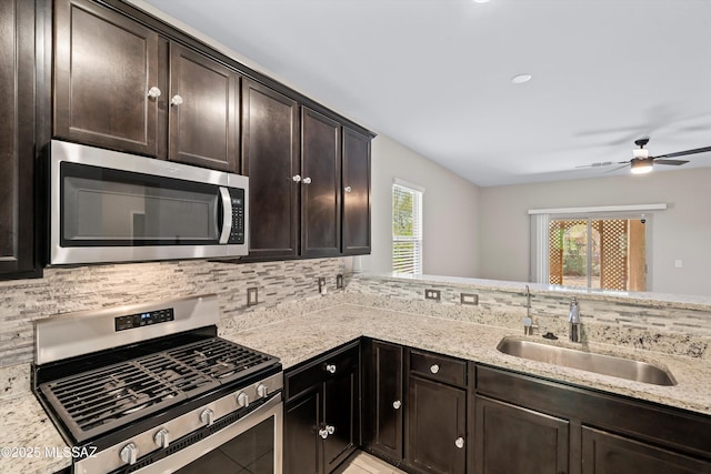 kitchen with a sink, backsplash, appliances with stainless steel finishes, light stone countertops, and dark brown cabinets