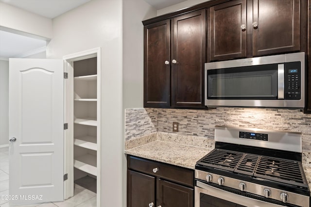 kitchen with tasteful backsplash, dark brown cabinets, light stone counters, light tile patterned flooring, and stainless steel appliances