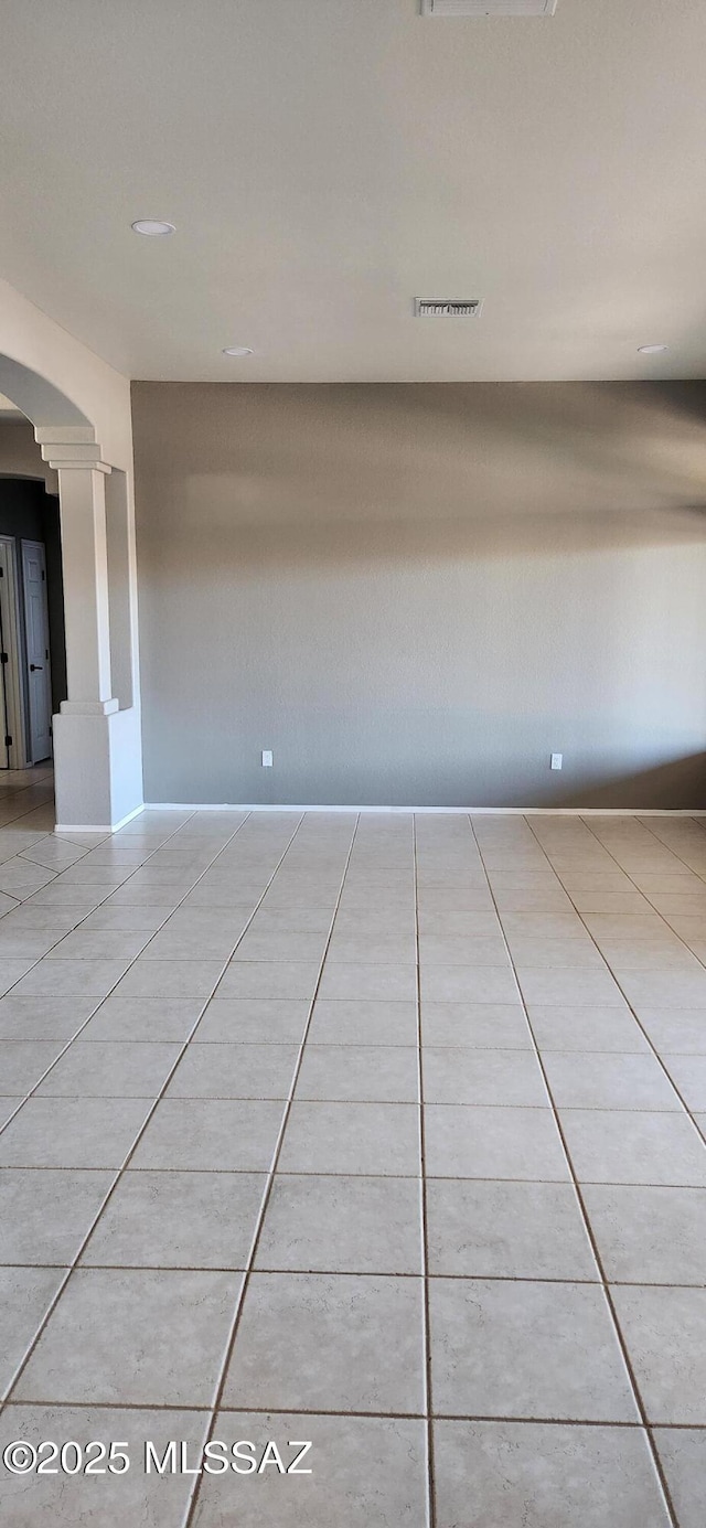 unfurnished room with arched walkways, tile patterned flooring, and ornate columns