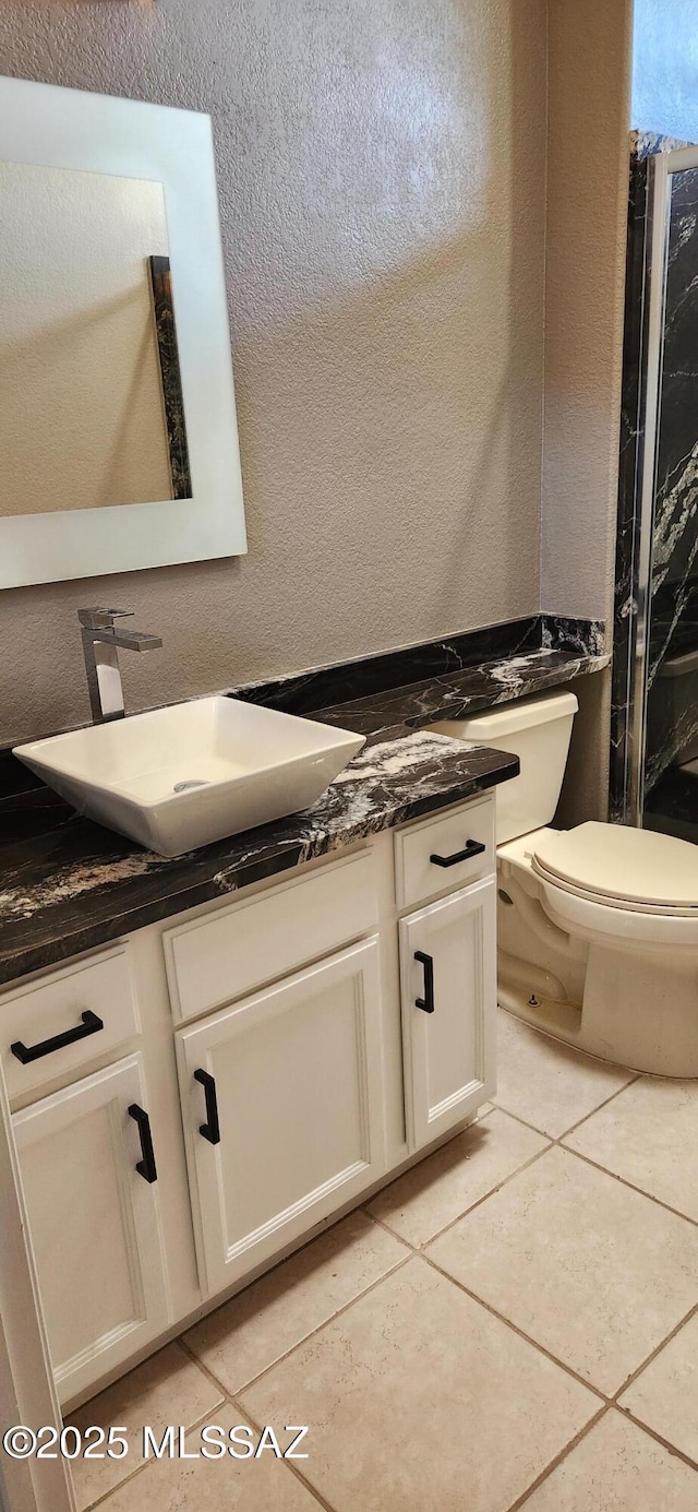 bathroom with toilet, a textured wall, tile patterned flooring, and vanity