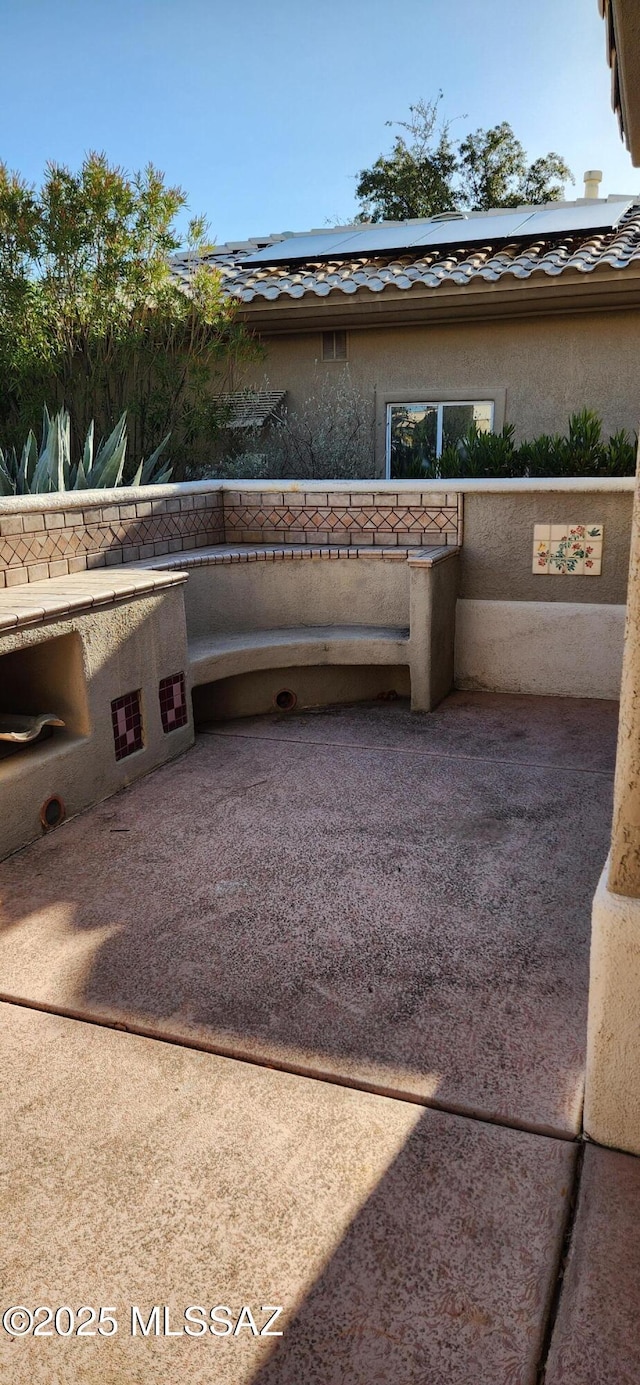 view of side of home with a tiled roof, roof mounted solar panels, a patio, and stucco siding