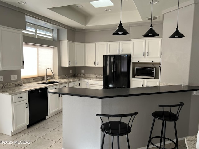 kitchen with visible vents, a raised ceiling, black appliances, a kitchen bar, and a sink