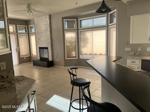 kitchen featuring light tile patterned floors, ceiling fan, a stone fireplace, and white cabinetry