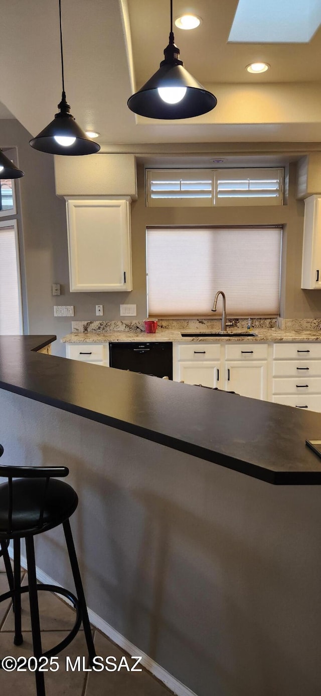 kitchen featuring black dishwasher, white cabinets, a breakfast bar, a sink, and recessed lighting