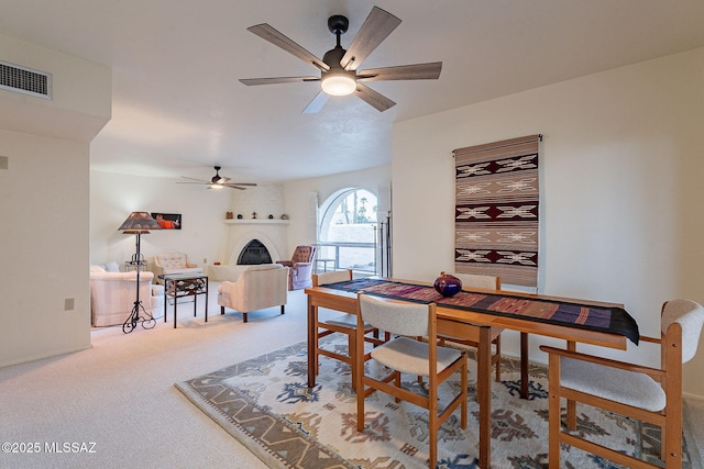 carpeted dining space with ceiling fan, a fireplace, and visible vents