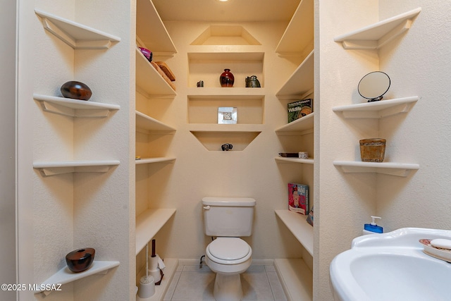 bathroom featuring toilet, built in shelves, a sink, and tile patterned floors