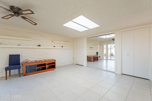 interior space with a textured ceiling, ceiling fan, light tile patterned floors, and a skylight