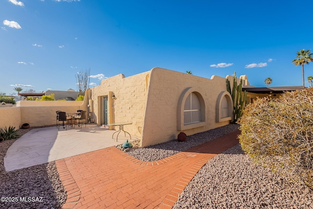 view of side of property featuring stucco siding, fence, and a patio