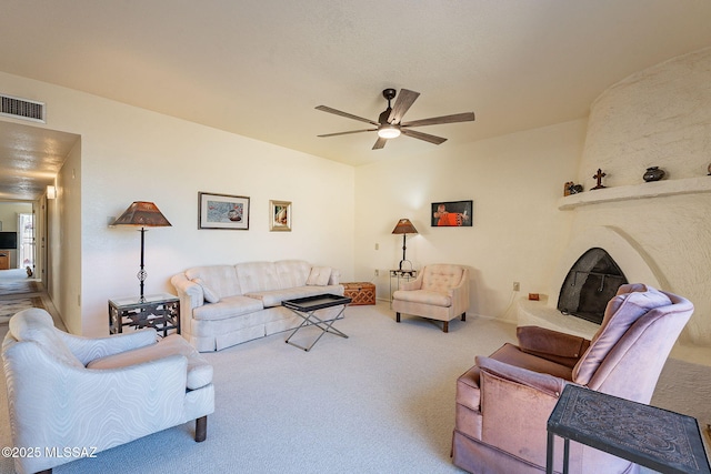 carpeted living area with a large fireplace, ceiling fan, and visible vents