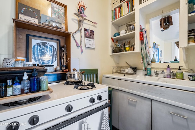 kitchen with gray cabinetry, a sink, open shelves, light countertops, and white gas range