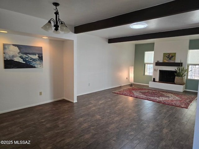 unfurnished living room featuring wood finished floors, baseboards, a fireplace with raised hearth, beamed ceiling, and a notable chandelier