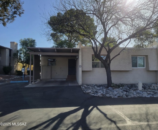 view of front facade with a carport, stucco siding, driveway, and fence