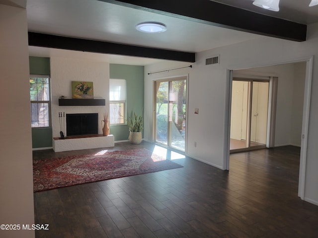 unfurnished living room with visible vents, beam ceiling, dark wood-type flooring, a large fireplace, and baseboards