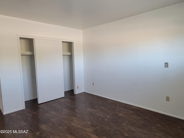 unfurnished bedroom featuring dark wood-style floors, a closet, and baseboards