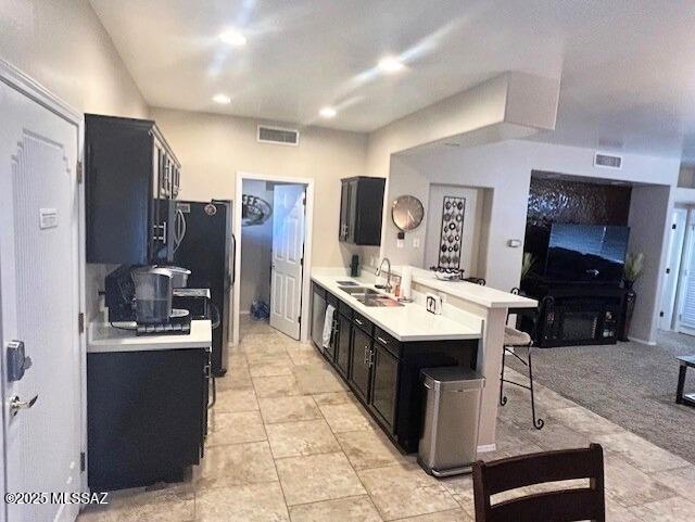 kitchen featuring visible vents, a breakfast bar, light countertops, a peninsula, and a sink