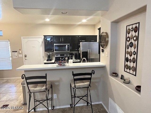 kitchen featuring stainless steel appliances, a breakfast bar, dark cabinets, and light countertops