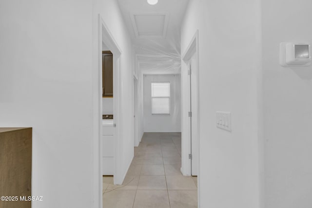 hall featuring light tile patterned floors and attic access