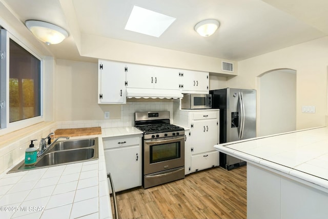 kitchen featuring tile countertops, stainless steel appliances, ventilation hood, and visible vents