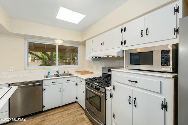 kitchen with light wood finished floors, decorative backsplash, appliances with stainless steel finishes, range hood, and a sink