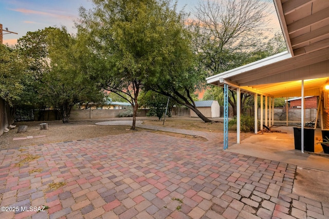 patio terrace at dusk with a storage unit, an outdoor structure, and a fenced backyard